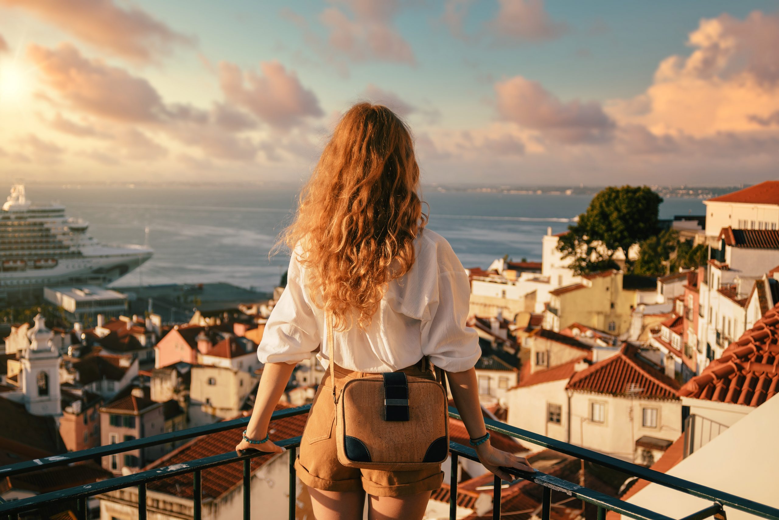 A young female tourist standing on a platform surrounded by fences and observing Lisbon at daytime in Portugal